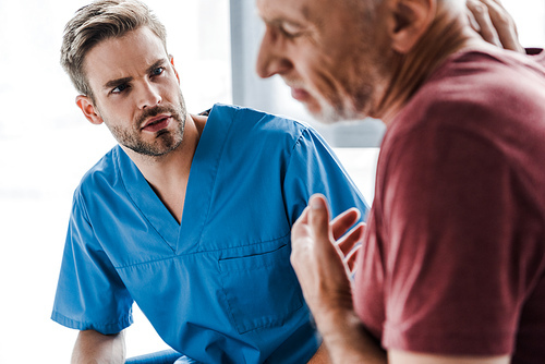 selective focus of handsome doctor looking at man in clinic