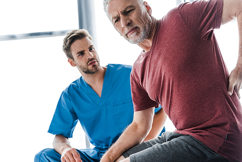 selective focus of man suffering from pain near doctor in clinic