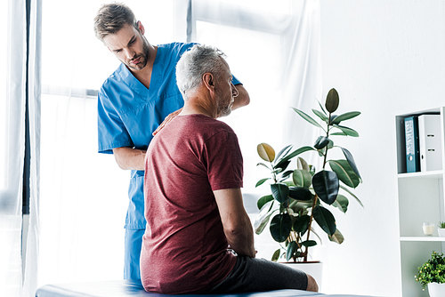 handsome chiropractor standing near mature patient