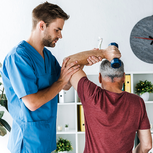 back view of middle aged man exercising with dumbbell near handsome doctor