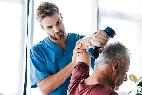 selective focus of doctor near middle aged man exercising with dumbbell