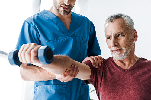 cropped view of doctor standing near mature man holding dumbbell