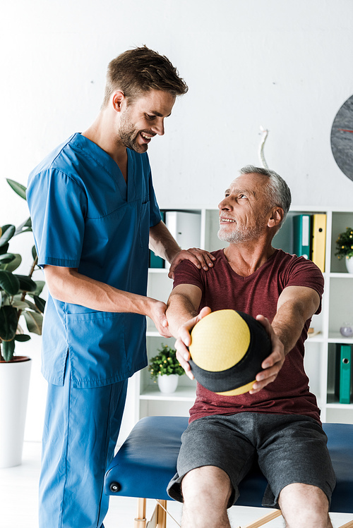 happy mature man looking at doctor while exercising with ball