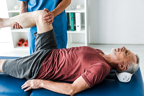 cropped view of doctor holding leg of mature man with closed eyes