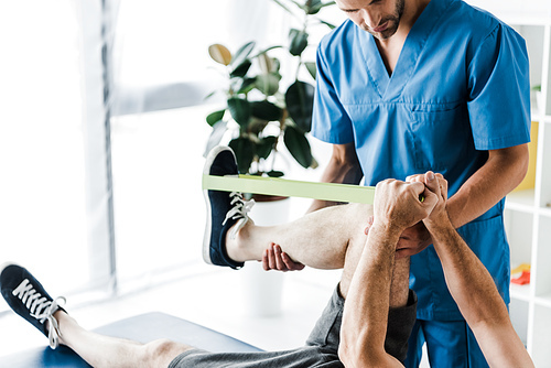 cropped view of doctor holding leg on mature man training with suspension straps