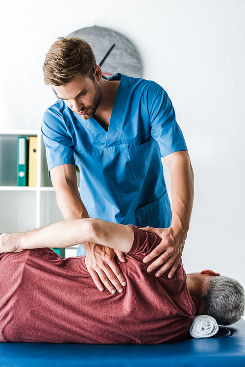 handsome doctor touching mature man lying on massage table