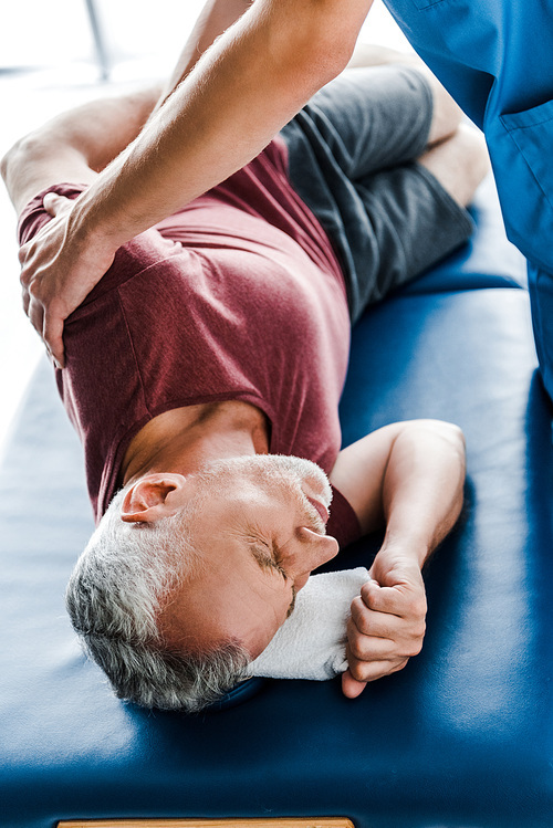 selective focus of doctor touching middle aged man with closed eyes lying on massage table