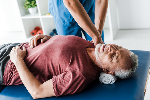 cropped view of doctor touching middle aged patient with closed eyes in clinic