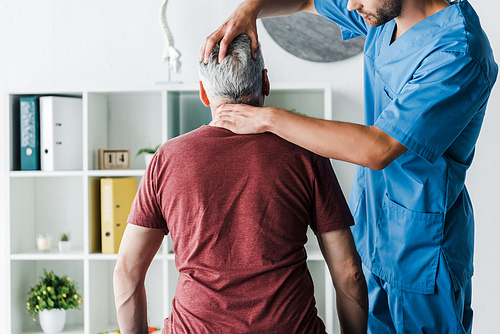 cropped view of bearded doctor touching head of middle aged patient in clinic