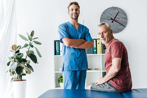 handsome doctor standing with crossed arms near happy patient