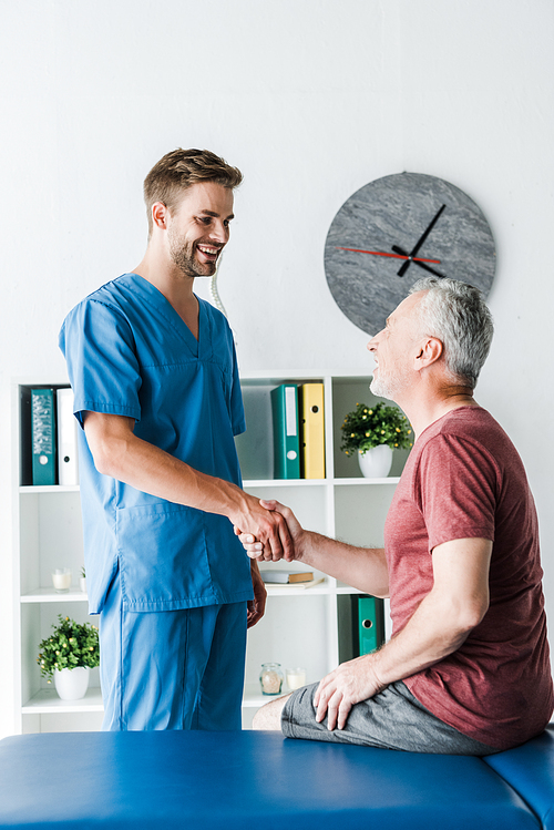 happy doctor shaking hands with cheerful mature patient in clinic