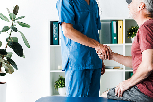 cropped view of doctor shaking hands with cheerful mature patient in clinic