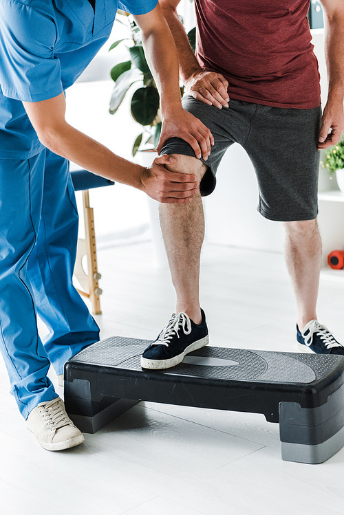 cropped view of doctor touching knee of mature patient on step platform