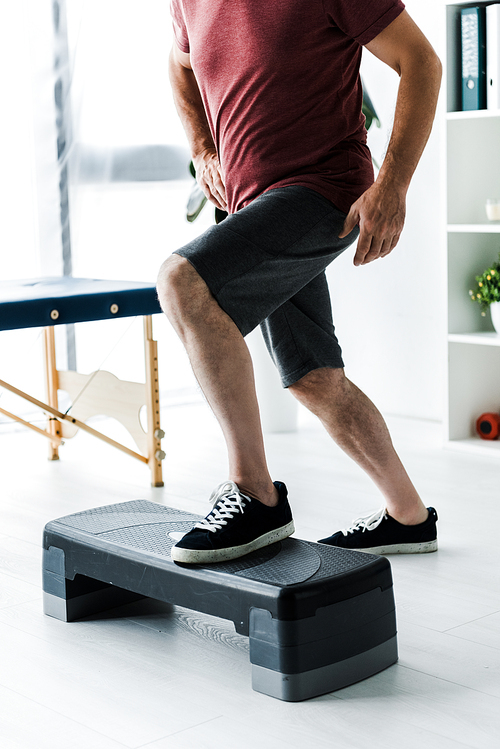 cropped view of middle aged man exercising on step platform in clinic