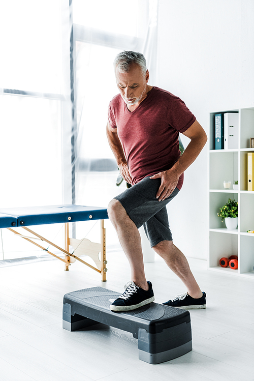 middle aged man exercising on step platform in clinic