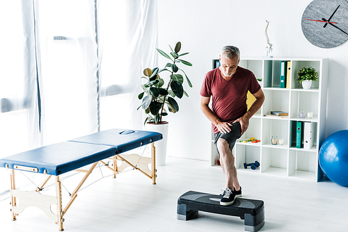 bearded mature man exercising on step platform in clinic