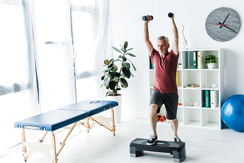 bearded mature man exercising with dumbbells in clinic