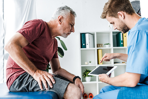 handsome doctor pointing with finger at digital tablet near patient