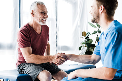 selective focus of happy patient shaking hands with doctor