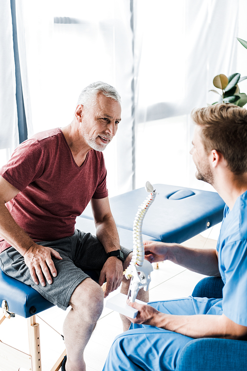 happy patient looking at doctor holding spine model