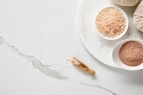 top view of clay powder and 씨솔트 in white bowls on marble table near wooden spatula