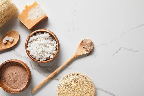 top view of clay powder and 씨솔트 in wooden bowls on marble table near spoons, soap and loofah