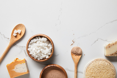 top view of clay powder and 씨솔트 in wooden bowls on marble table near spoons, soap and organic loofah