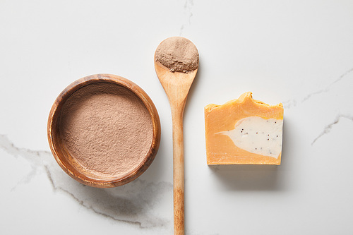 top view of clay powder in bowl and spoon near natural soap on marble table