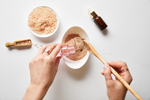 cropped view of woman adding liquid to clay powder while preparing organic cosmetics