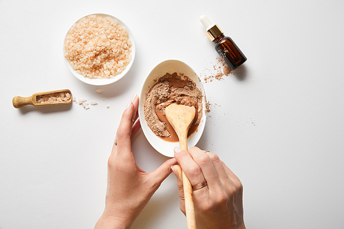 cropped view of woman mixing clay in bowl with wooden spoon near 씨솔트 and oil on marble table