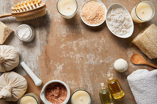 top view of natural cosmetic ingredients and beauty supplies near decorative candles on textured weathered beige surface