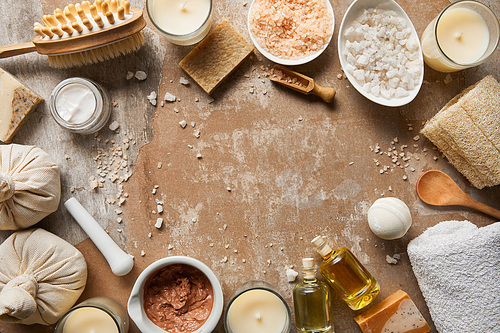 top view of natural cosmetic ingredients and beauty supplies near decorative candles on textured weathered beige background