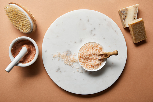 top view of clay, wooden massage brush and soap on beige background near 씨솔트 in bowl on marble circle