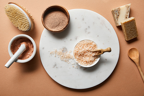 top view of clay, wooden massage brush, spoon and soap on beige background near 씨솔트 in bowl on marble circle