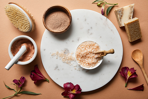 top view of organic cosmetic ingredients on beige background and marble circle near scattered flower petals