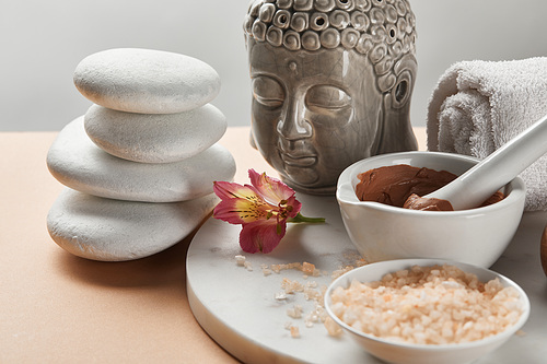 clay and 씨솔트 in bowl near buddha figurine and spa stones on marble circle isolated on grey