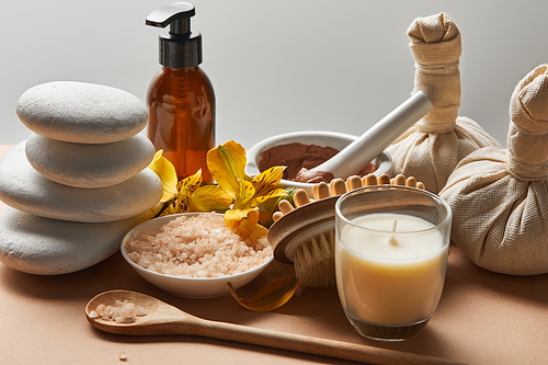 spa cosmetics, stones, massage brush, candle and yellow flowers on beige surface isolated on grey