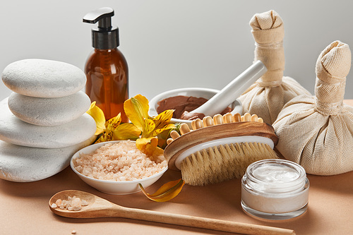 various spa cosmetics, stones, massage brush, candle and yellow flowers on beige surface isolated on grey