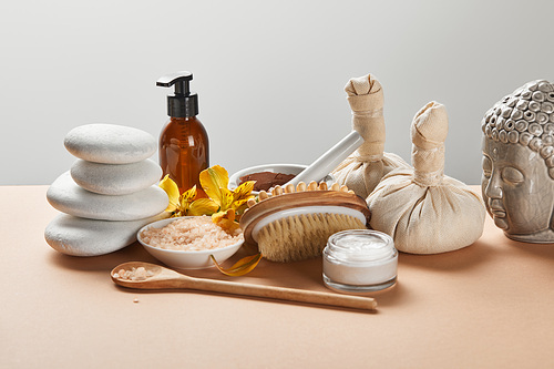 spa cosmetics, stones, massage brush, candle, Buddha figurine and yellow flowers on beige surface isolated on grey