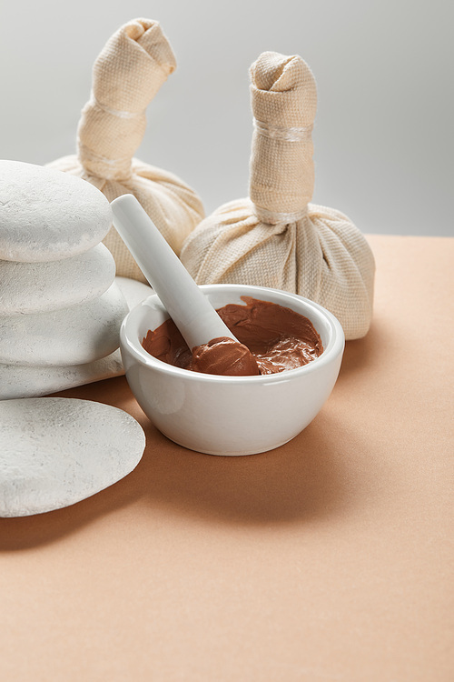 clay in bowl near stones on beige surface isolated on grey