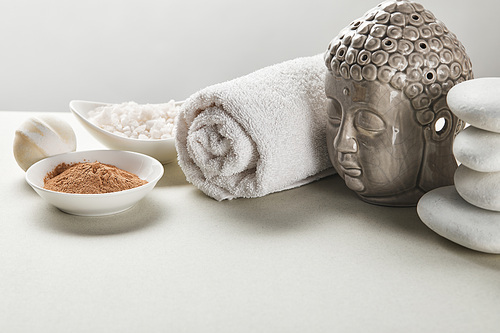 씨솔트 and clay powder in bowls, cotton towel, stones, bath bomb and buddha figurine on white table isolated on grey