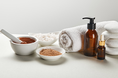 씨솔트 and clay in bowls, cotton towel, stones, bottles on white table isolated on grey