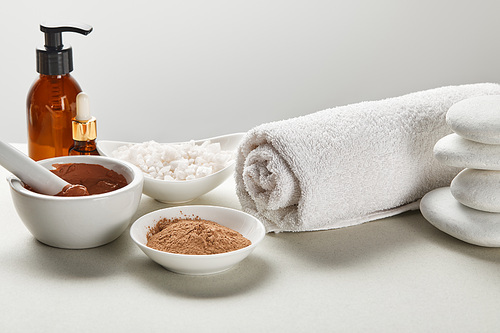 씨솔트 and clay in bowls, cotton towel, stones, bottles on white surface isolated on grey