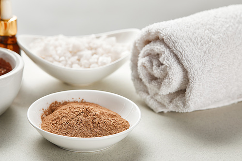 selective focus of clay powder and 씨솔트 in bowls near white rolled cotton towel isolated on grey