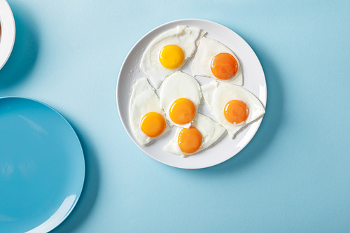 top view of fried eggs on white plate on blue background