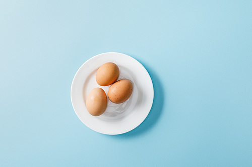 top view of fresh eggs on white plate on blue background