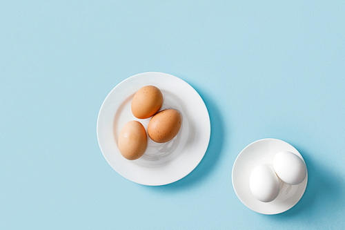 top view of fresh brown and white eggs on white plates on blue background