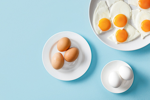 top view of fresh boiled and fried eggs on white plates on blue background