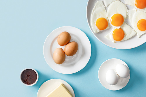 top view of boiled and fried eggs, jam and butter on blue background