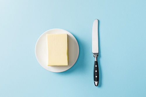 top view of butter on white plate and knife on blue background